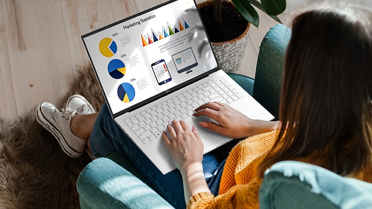 A person sitting comfortably in a chair, using a laptop that displays a presentation with charts and graphs. An animation demonstrates the anti-glare screen by showing no light reflection even when sunlight shines directly onto the display.