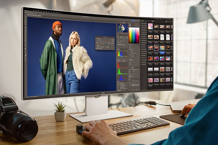 A guy is working with design program on UltraFine Monitor. A camera is placed next to the monitor.