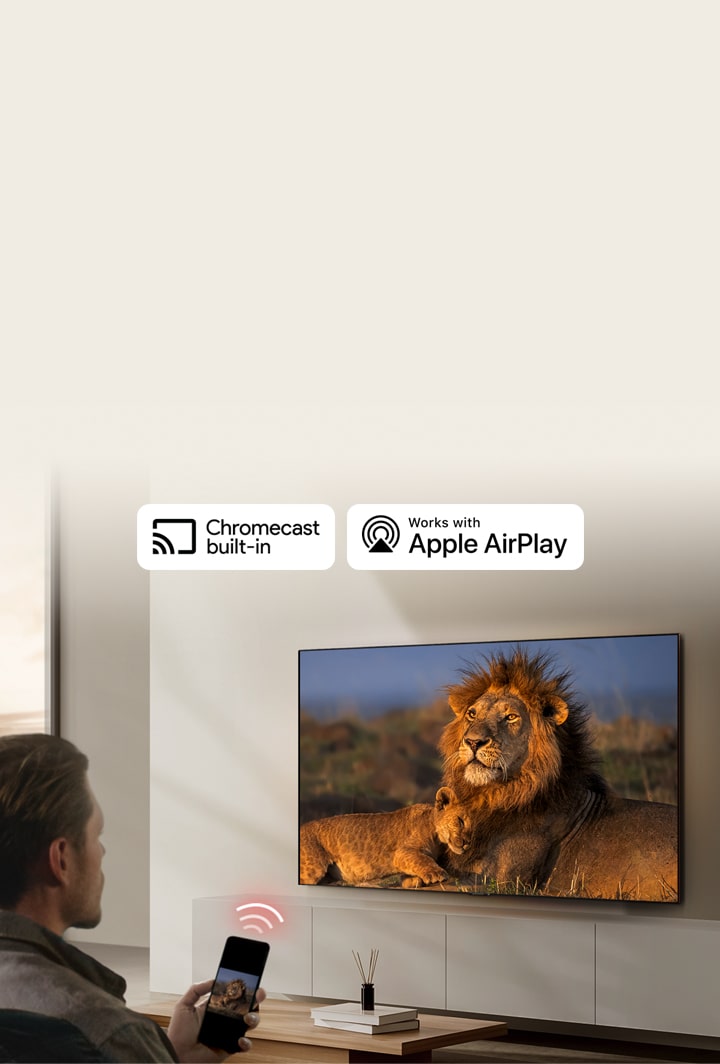 Uma TV LG montada na parede de uma sala de estar exibindo um leão e um filhote de leão. Um homem está sentado em primeiro plano com um smartphone na mão exibindo a mesma imagem de leões. Um gráfico de três barras curvas vermelhas neon é exibido logo acima do smartphone apontando para a TV.