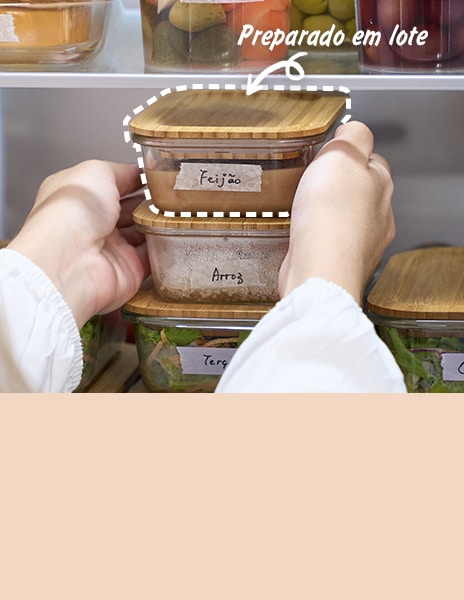 Mãos colocando refeições preparadas em recipientes transparentes.