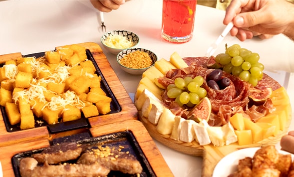 Exibição de alimentos e bebidas de festa como queijo, salame e frutas.