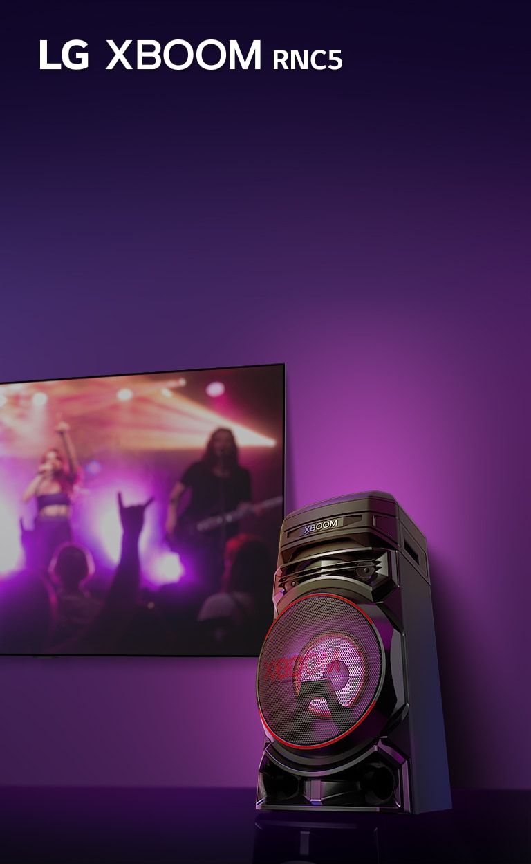 Uma visão de baixo ângulo do lado direito do LG XBOOM RNC5 contra um fundo roxo. A luz do XBOOM também é roxa. E uma tela de TV exibe uma cena de concerto.