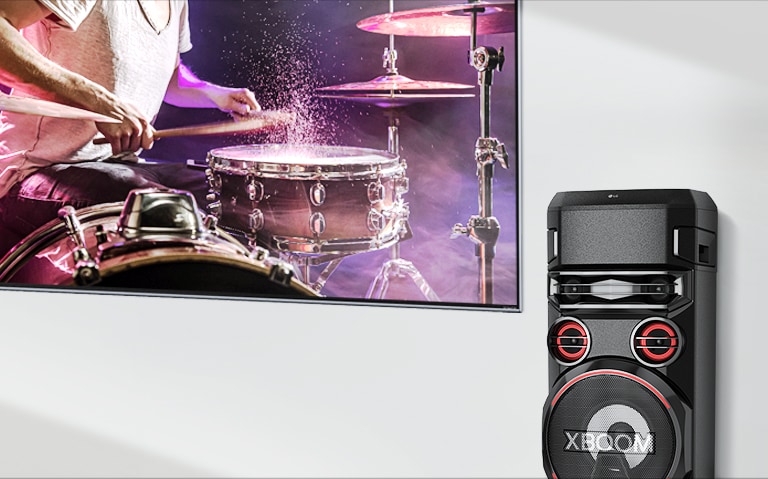 A TV está em uma parede com uma CAIXA ACÚSTICA LG XBOOM à direita.