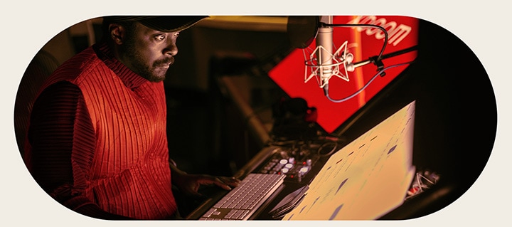 will.i.am está trabalhando no estúdio olhando para uma tela posicionada abaixo de um microfone.
