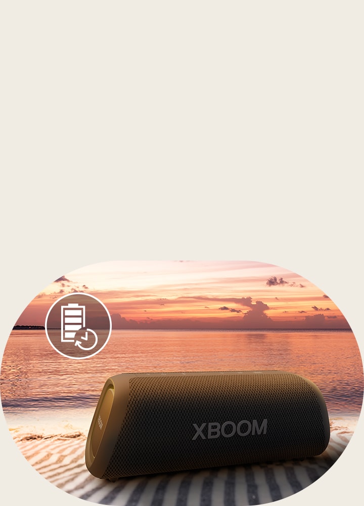 A caixa de som está colocada sobre uma toalha de praia. Na frente dela, vê-se uma praia ao pôr do sol para ilustrar que a caixa de som pode ficar ligada por até 24 horas.