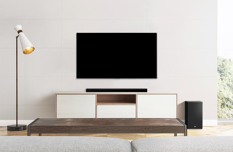 Uma TV, barra de som e subwoofer colocados em uma sala de estar simples.