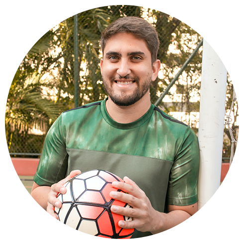 Especialista em edição Enzo Gardini segurando uma bola com um grande sorriso no rosto. Ele tem uma barba e está usando uma camiseta verde.