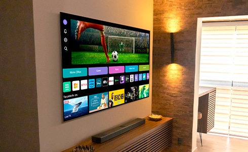 TV LG OLED pendurada na parede, operando com webOS na tela. Vários ícones de plataforma e serviço na tela do webOS.