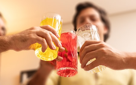 Três amigos brindando com copos de bebidas na festa. Bebida amarela, vermelha, branca com gelo.