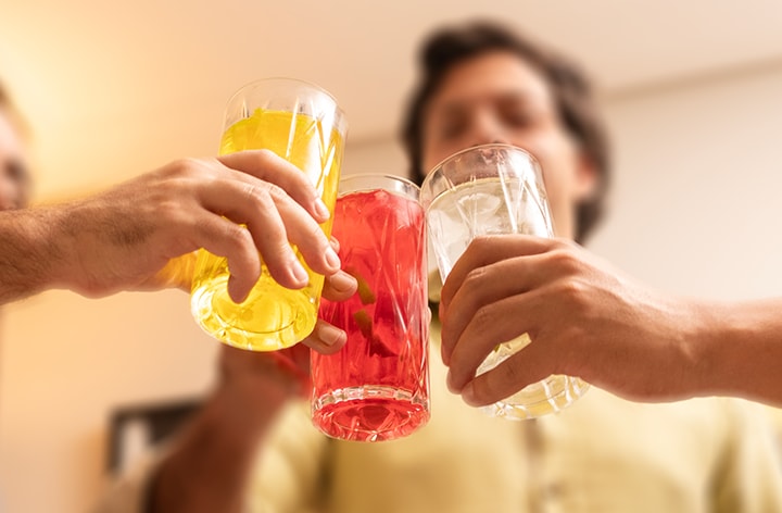 Três amigos brindando com copos de bebidas na festa. Bebida amarela, vermelha, branca com gelo.