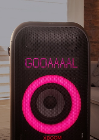 Alto-falante XBoom exibindo cor rosa na tela circular e texto dizendo 'GOOAAAAL' conforme o usuário configurou via aplicativo móvel.