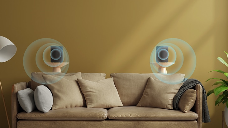 Dois alto-falantes traseiros estão posicionados em uma mesa lateral atrás do sofá, com um efeito sonoro virtual que sugere a propagação do som para a frente.