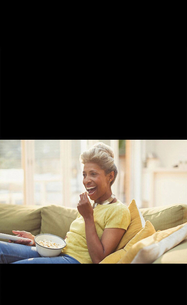 Uma mulher vê TV segurando um controle remoto. Ela também está comendo pipoca