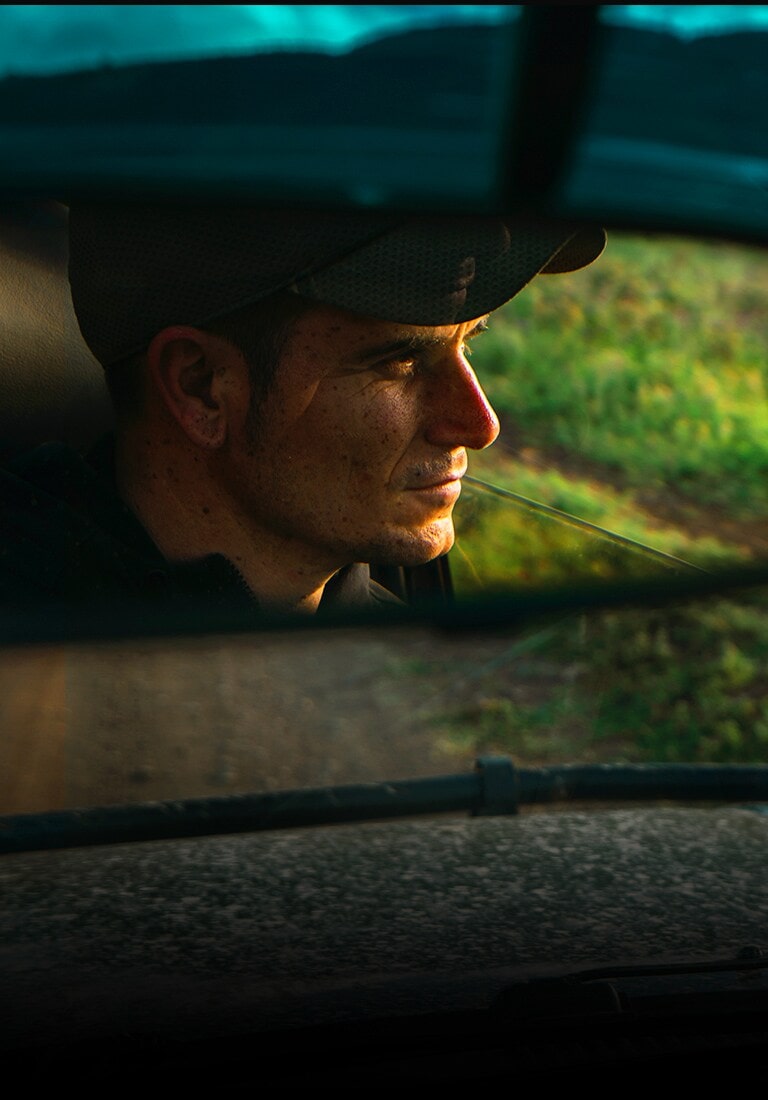 Reflexo de um homem no espelho retrovisor do carro. O zoom se afasta para mostrar a mesma cena na TV QNED.