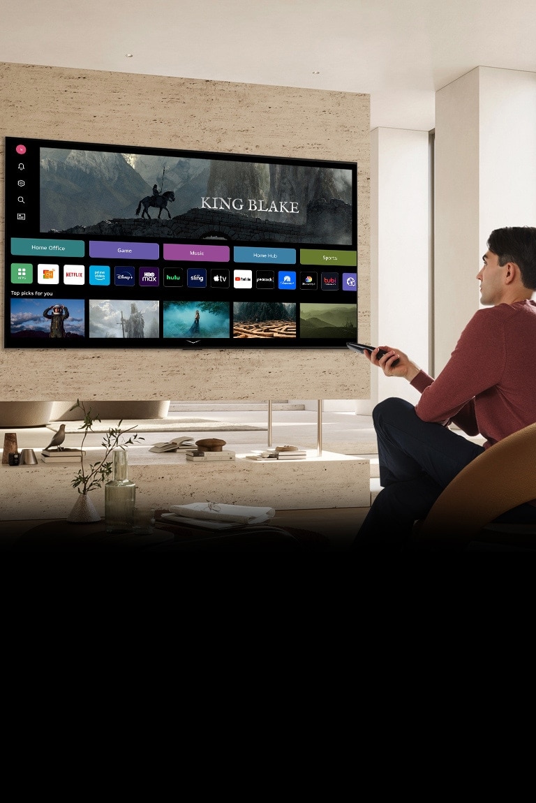Um homem está segurando um controle remoto na mão direita e olhando para uma grande TV à sua frente. A TV exibe a tela inicial totalmente renovada.