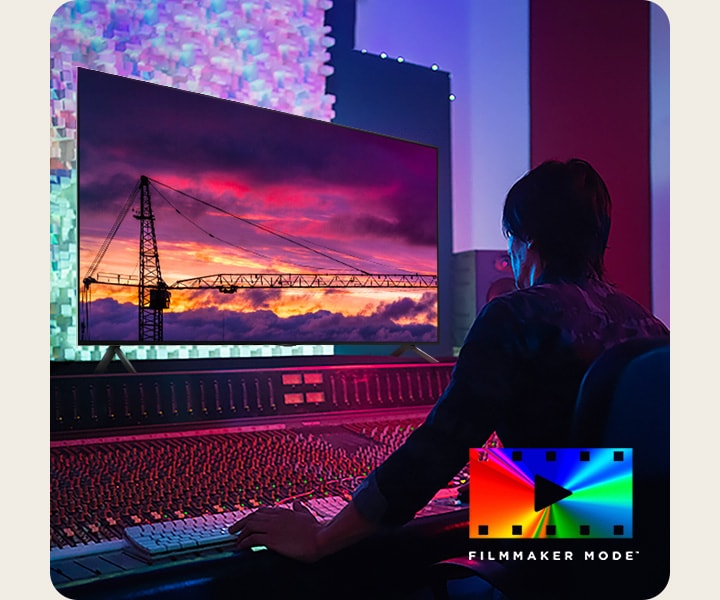 Um homem em um estúdio de edição escuro olhando para uma TV LG exibindo o pôr do sol. No canto inferior direito da imagem está o logotipo do FILMMAKER Mode.