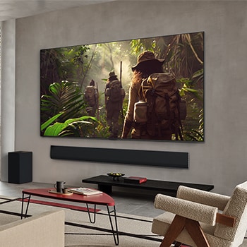 Wide view of a living room inside a premium home, a man is watching a movie on his wall-mounted LG OLED TV. The TV's design blends elegantly with the wall and the interior design.