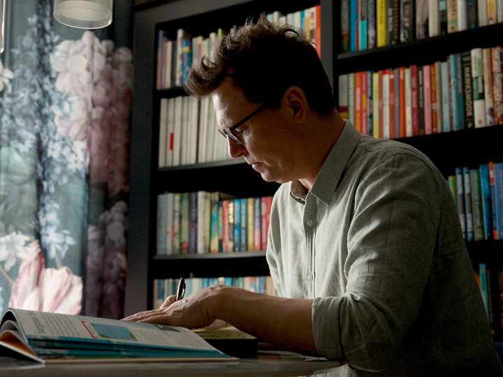 'A cameraman in glasses sitting in a softly lit home setting, sharing his thoughts on camera