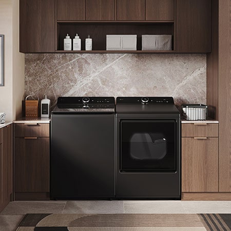 The LG Top Load Washer and Dryer set (WT8600CB) in Black Steel, showcasing its premium, side-by-side design seamlessly integrated into a luxurious laundry room with marble and wood finishes.