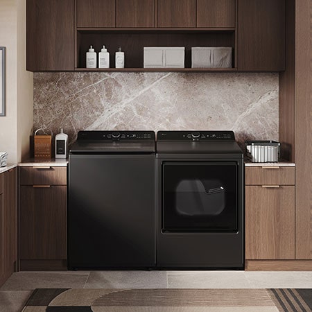 The LG Top Load Washer and Dryer set (WT8400CB) in Black Steel, showcasing its premium, side-by-side design seamlessly integrated into a luxurious laundry room with marble and wood finishes.
