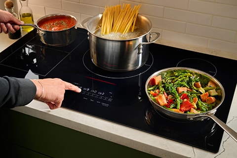 User boiling pasta and stir-frying vegetables on an LG induction cooktop, highlighting rapid heat response and precise temperature control for efficient cooking.