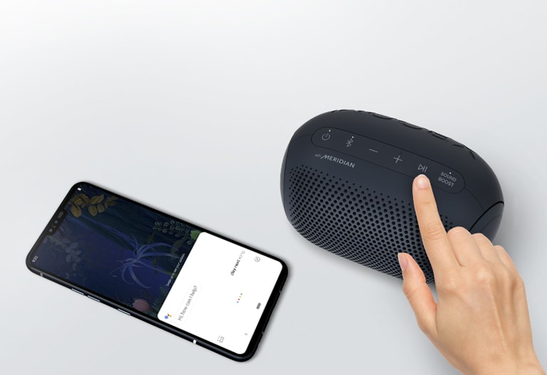 A hand presses a button on LG XBOOM Go. A smartphone is next it. There's a speech bubble. Google's logo is in the top right.