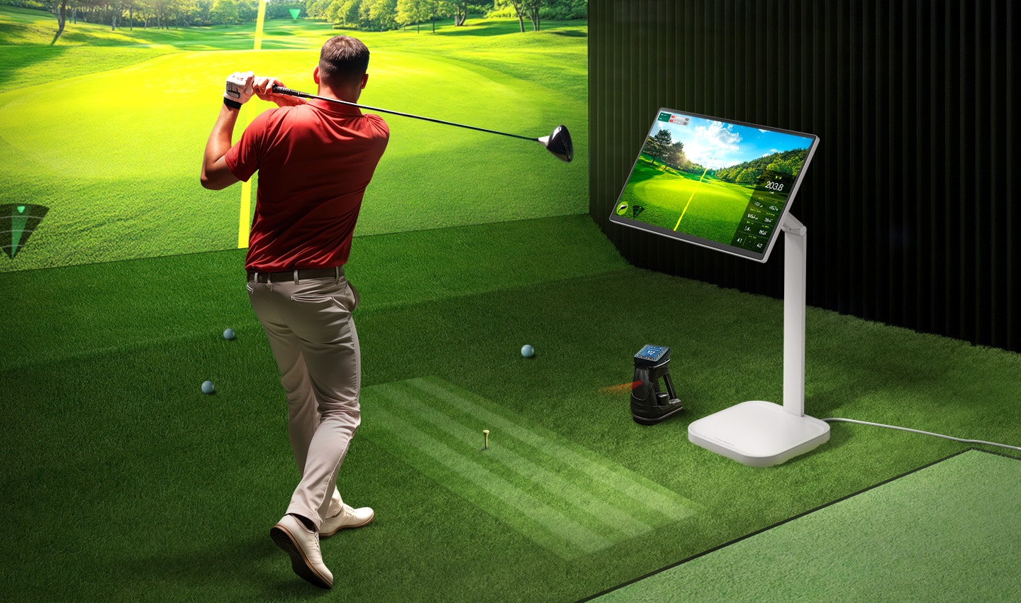 A man is playing golf at an indoor screen golf facility, with a LG Smart Monitor Swing next to him displaying data. A man is playing golf at an indoor screen golf facility, with a LG Smart Monitor Swing next to him displaying data.