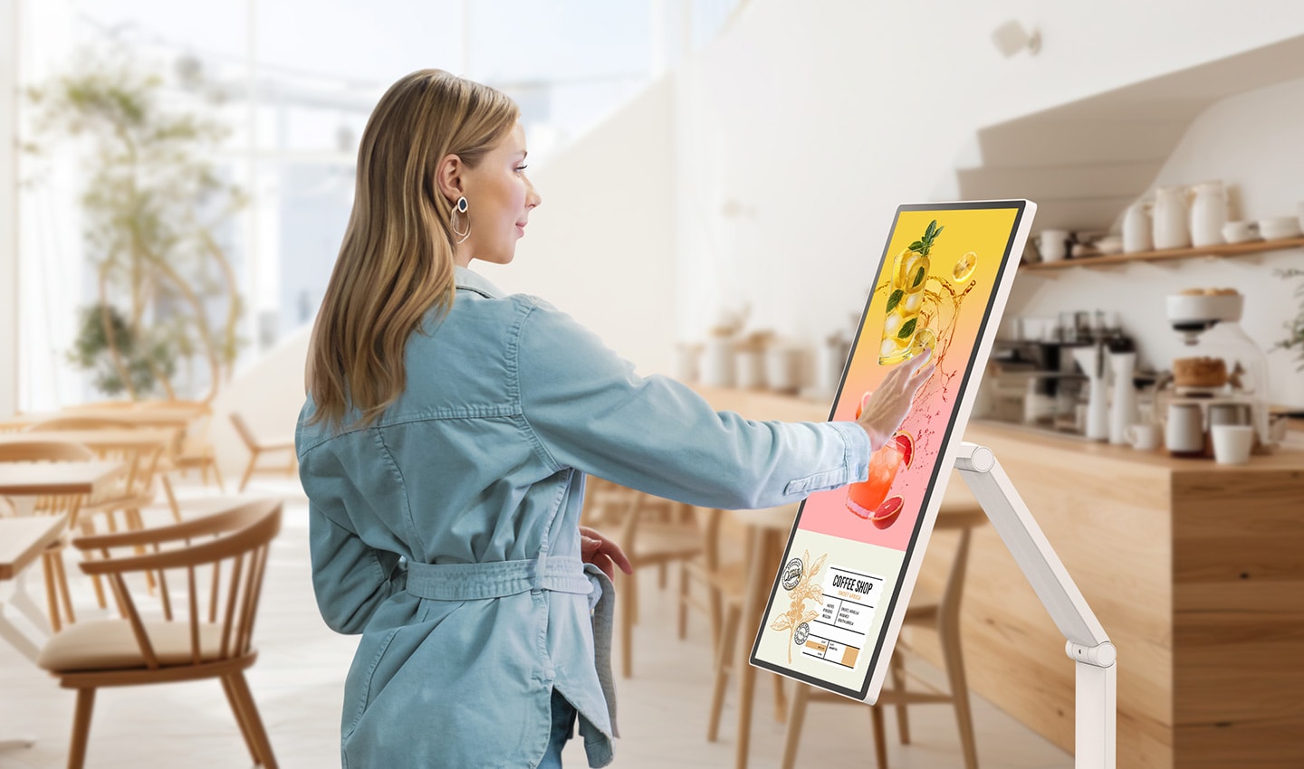 A woman is looking at an event banner displayed on a LG Smart Monitor Swing in a café. A woman is looking at an event banner displayed on a LG Smart Monitor Swing in a café.