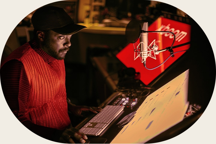 will.i.am is working in studio looking at a screen placed below a mic.