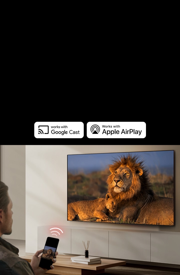 \An LG TV mounted on a wall in a living room, displaying a lion and lion cub. A man sits in the foreground with a smartphone in his hand displaying the same image of lions. A graphic of three neon red curved bars is displayed just above the smartphone pointing toward the TV.	