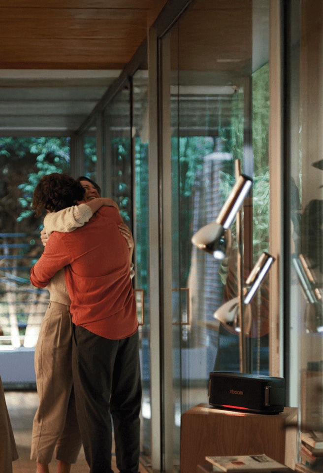 A woman and a man embrace in the living room, with the XBOOM speaker turned on beside them.