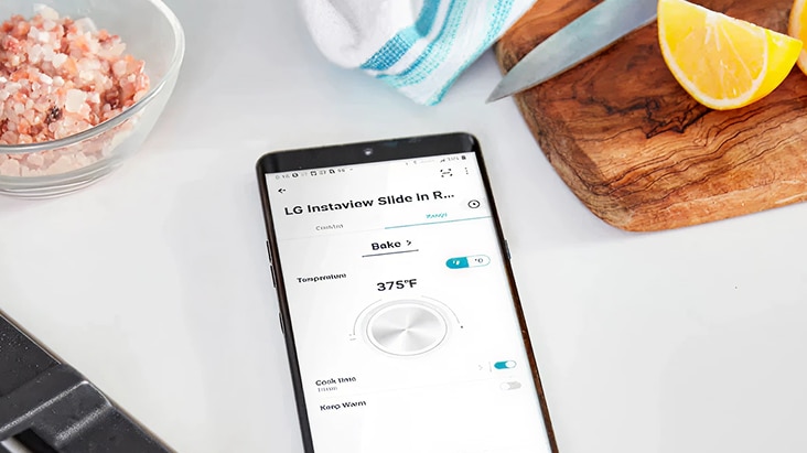 A smartphone displays the LG ThinQ app controlling the LG InstaView Slide-In Range oven, enabling efficient product maintenance in the kitchen.