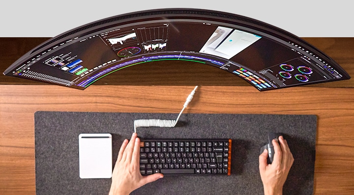 Person working at desk, hands navigating mouse and keyboard in front of a wide monitor.