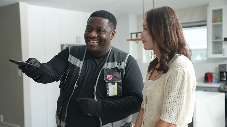 Technicien de LG souriant, expliquant quelque chose à un client dans une cuisine moderne et lumineuse, représentant le service à domicile de LG et les réparations à prix forfaitaire.