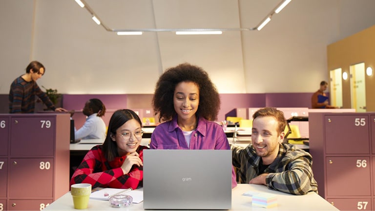 Trois personnes dans un bureau regardent un LG gram en souriant.