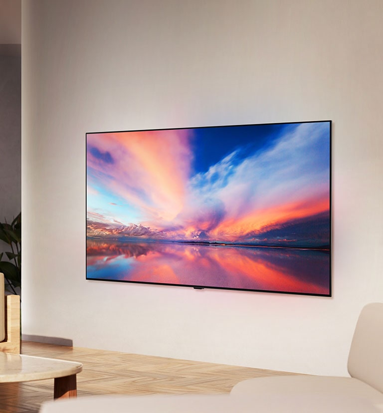 Un téléviseur OLED de LG, le modèle OLED B4, accroché au mur dans une pièce neutre affichant une photo colorée d’un coucher de soleil sur l’océan. 