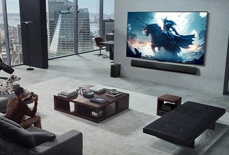 Wohnzimmer mit einer Person, die ein Video-Game auf einem an der Wand montierten LG True Wireless TV mit LG Soundbar spielt. Sie hält einen Controller in der Hand, aber die Spielkonsole ist nicht sofort zu sehen. Es sind auch keine Kabel zu sehen. Die Zero Connect Box steht versteckt unter einem Beistelltisch.