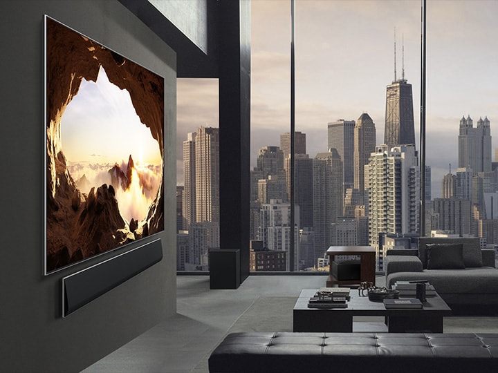 Geräumiges Wohnzimmer mit Blick auf eine Stadtlandschaft. Der LG OLED TV ist mit einer LG Soundbar an der Wand befestigt. Von der Seite betrachtet, fügen sich das flachbündige Design des Fernsehers und die ultra-schlanken Blenden gut in die Wand und den Raum ein. Die Zero Connect Box ist zu sehen, aber unauffällig aufgestellt.