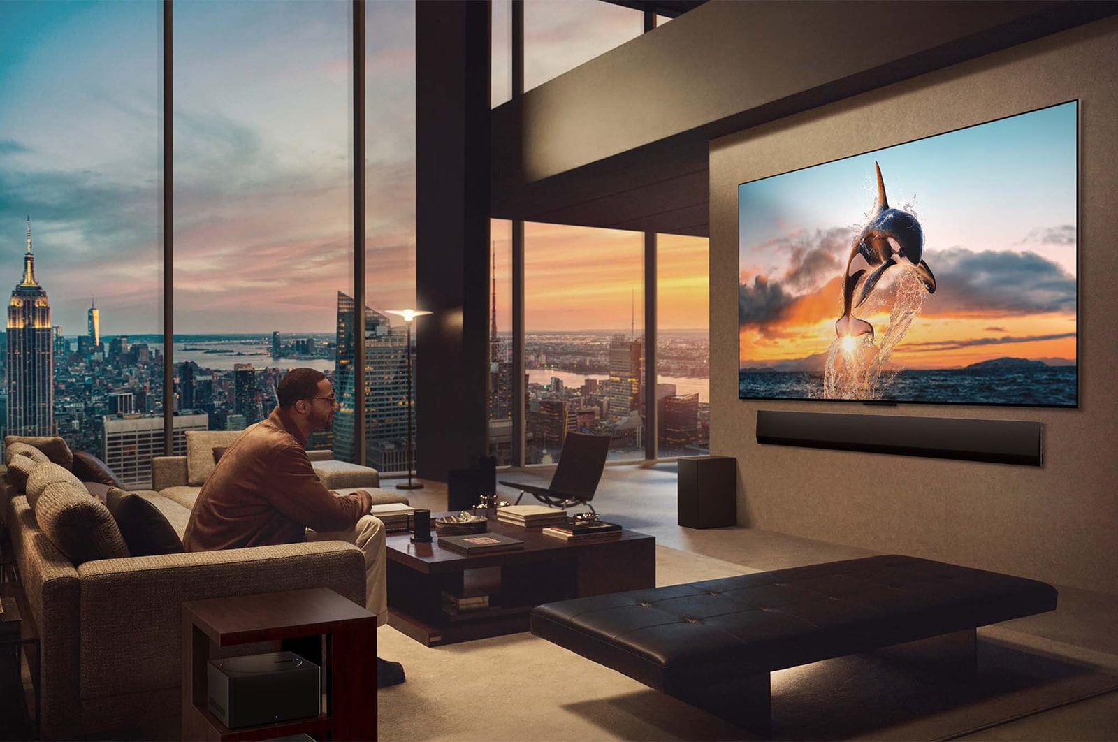 Geräumiges Wohnzimmer mit Blick auf eine Stadtlandschaft. Der LG OLED TV ist mit einer LG Soundbar an der Wand befestigt. Das flächenbündige Design des Fernsehers ermöglicht eine bündige Montage an der Wand und fügt sich gut in den Raum ein. Die Zero Connect Box ist zu sehen, aber unauffällig aufgestellt.