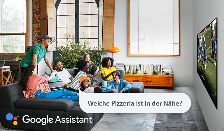 Eine Frau, die sich mit Freunden ein Fussballspiel im Fernsehen ansieht, fragt Google Assistant, welche Pizzeria sich in der Nähe befindet.