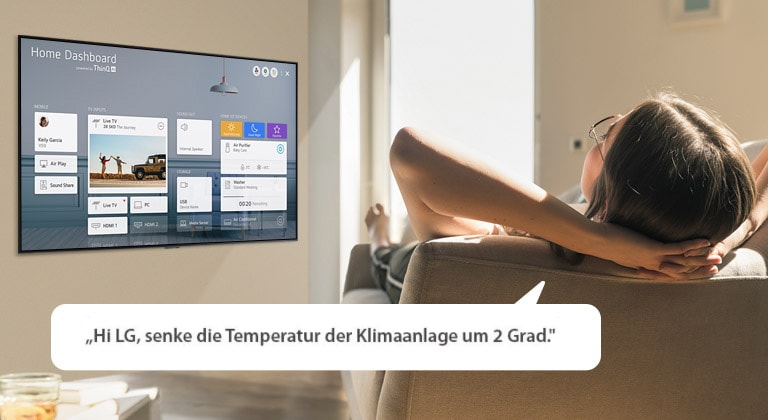 Frau, die auf einem Sofa liegt und den Fernseher per Sprachbefehl dazu auffordert, die Temperatur der Klimaanlage zu senken. Auf dem TV-Bildschirm ist das Home Dashboard zu sehen.