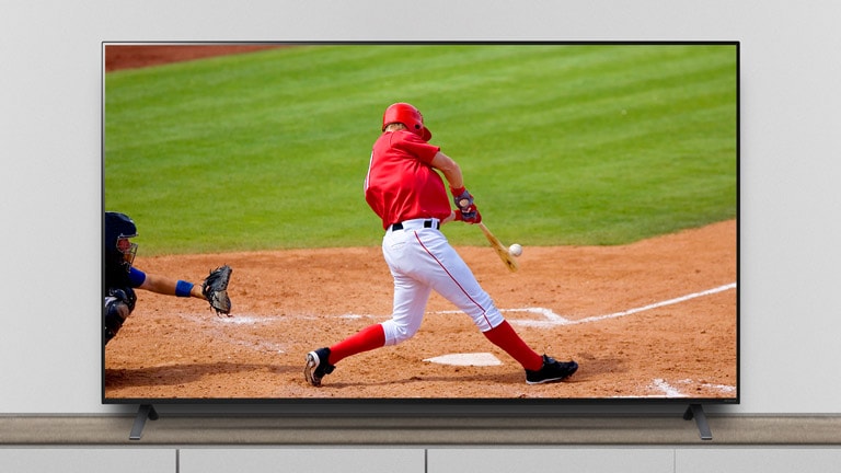 Der Fernseher steht auf dem Standfuss, und auf dem Bildschirm ist ein Baseballspiel zu sehen.