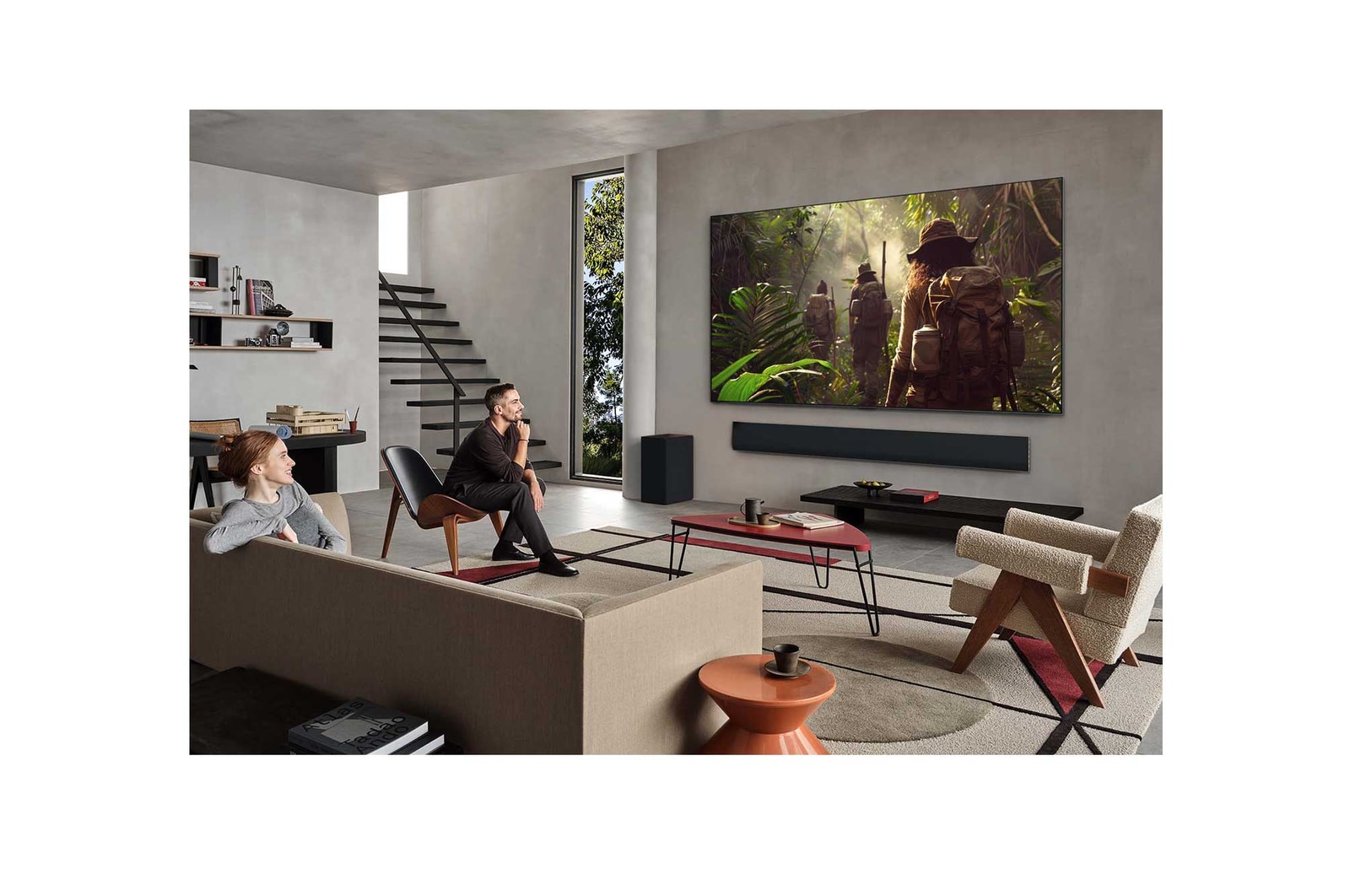 Weite Ansicht eines Wohnzimmers in einem hochwertigen Haus. Ein Mann sieht sich einen Film auf seinem an der Wand montierten LG OLED-Fernseher an. Das Design des Fernsehers fügt sich elegant in die Wand und die Inneneinrichtung ein.