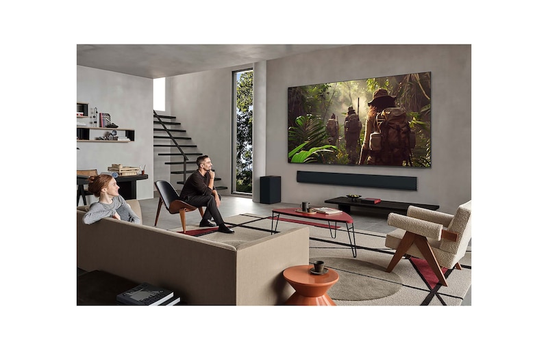 On an LG OLED TV screen is the webOS 25 home page filled with apps and entertainment content. By the TV is the LG AI Magic Remote, the AI button is highlighted as if activated by the user's voice. A speech bubble is beside it, switching to my account. The short text explains how users can now synchronize their voice to their personal profile for easier navigation and personalized recommendations.
