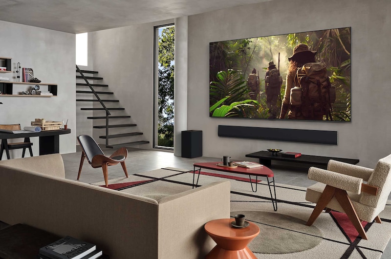 On an LG OLED TV screen is the webOS 25 home page filled with apps and entertainment content. By the TV is the LG AI Magic Remote, the AI button is highlighted as if activated by the user's voice. A speech bubble is beside it, switching to my account. The short text explains how users can now synchronize their voice to their personal profile for easier navigation and personalized recommendations.