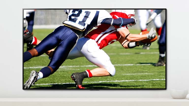 Szene aus einem American-Football-Spiel mit zwei rangelnden Spielern auf einem Fernsehbildschirm