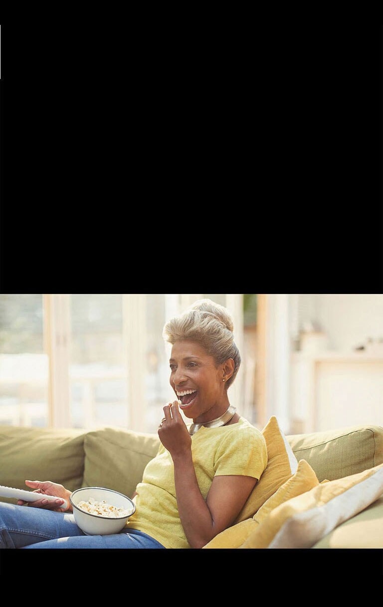 Une femme regarde le téléviseur – tenant une télécommande. Elle mange également du pop-corn.