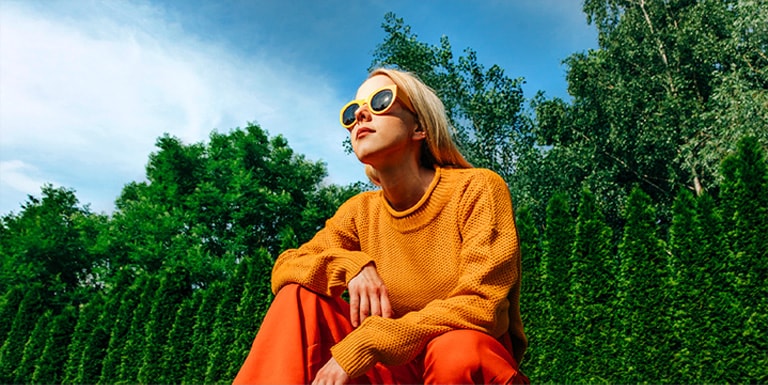 Une femme accroupie à l’extérieur par une journée ensoleillée devant des arbres et un ciel bleu dans une cour, image pixelisée. La cartographie des tons et l’effet d’amélioration de l’expression s’appliquent à la femme, rendant la zone plus lumineuse. L’arrière-plan est ensuite scanné, ce qui le rend plus lumineux.