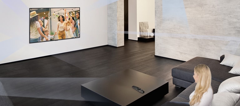 Une femme dans un grand salon à la décoration minimaliste regarde des gens danser sur un téléviseur.