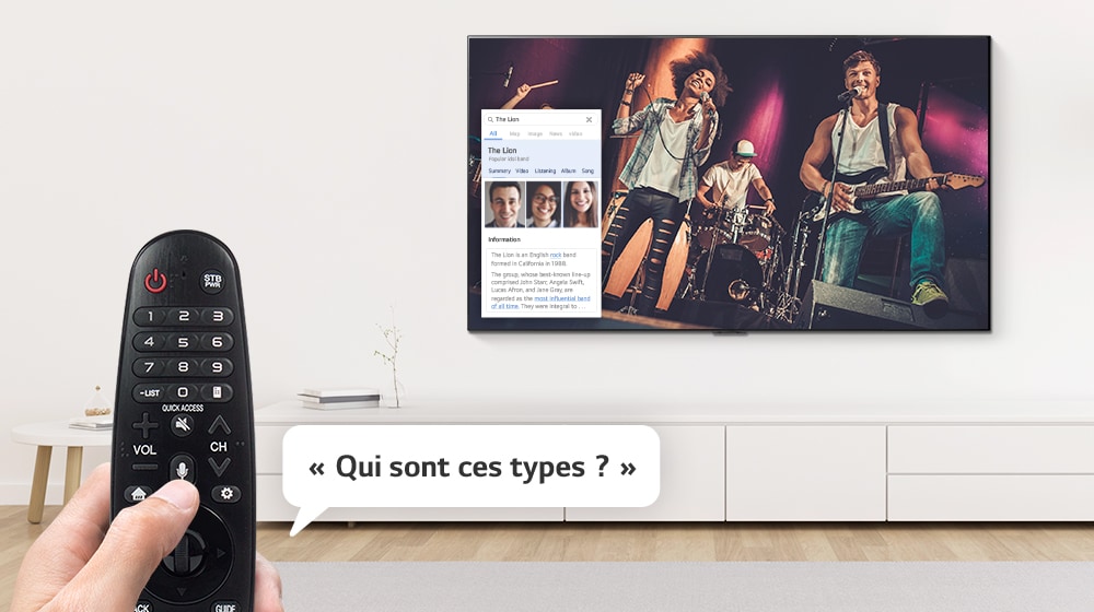 Gros plan d’une main qui contrôle le téléviseur avec une télécommande pour demander qui sont les types qui chantent à l’écran.
